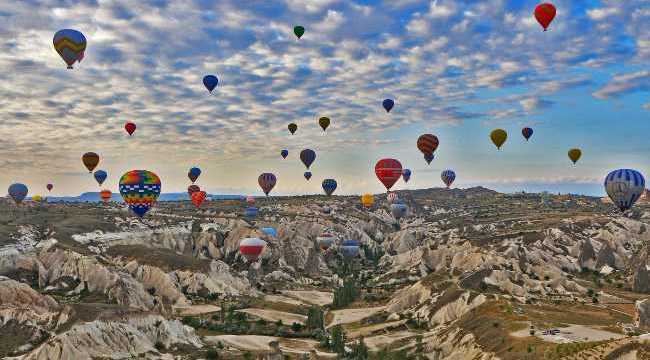 many colorful hot air balloons flying over Cappadocia’s fairy chimneys